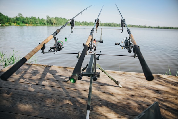 Young fisherman fishing on lake or river. Front view of three fishing rods standing on water pier without people. Empty place with sunshine and beautiful weather. Fishing time.