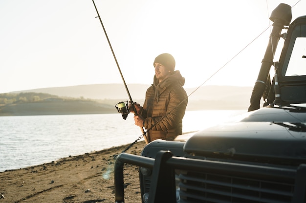 Young fisherman standing near his car and holding fishing equipment