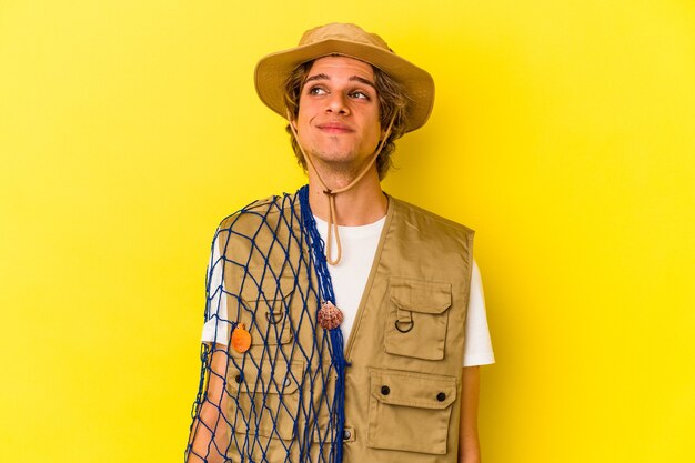 Young fisherman with makeup holding a net isolated on yellow background  dreaming of achieving goals and purposes