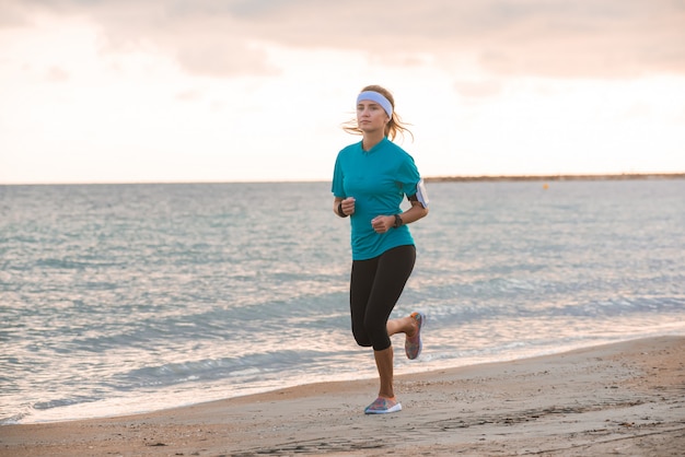 Young fit girl running on beach at sunrise in morning