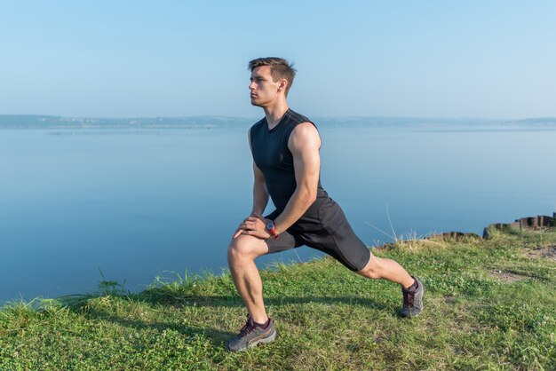 Young fit man stretching legs outdoors doing forward lunge.