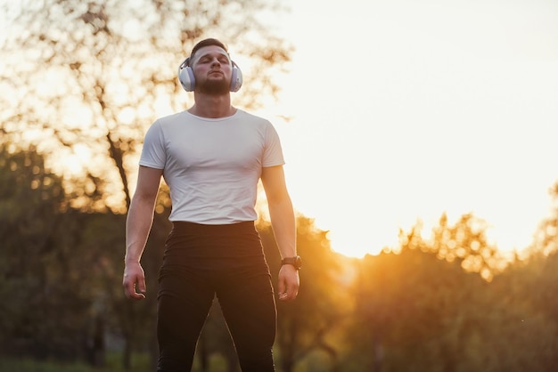 Young fit man with closed eyes in sportswear listening to music while resting after a run or workout