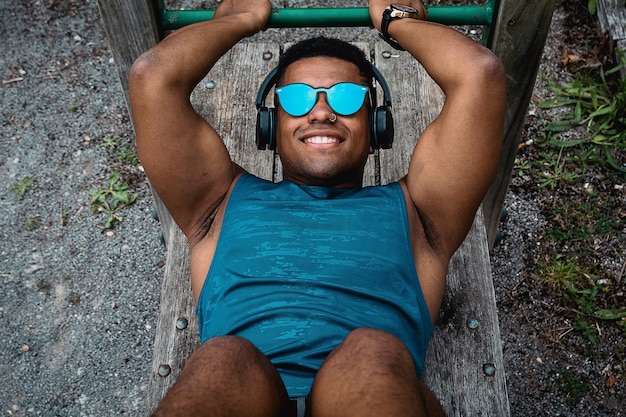 Young fit man with sunglasses and a blue shirt working out in the park while listening to music