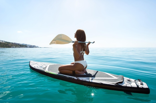 Young fit sexy woman in a swimsuit poses with a sup board Sup surfing