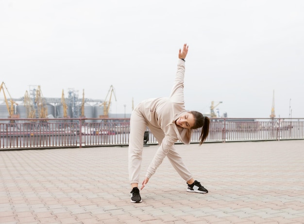 Young fit slim woman doing warmup exercise before training outdoors