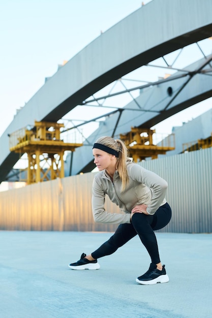 Young fit sportswoman in sneakers leggins and sport jacket exercising outdoors