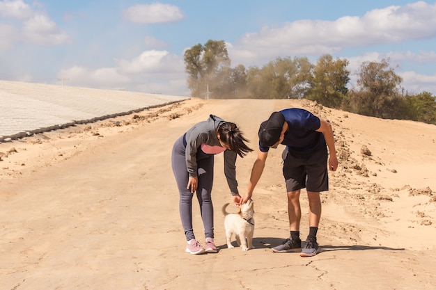 Young fitness couple petting their small dog in the sand.