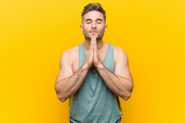 Photo young fitness man against a yellow  holding hands in pray near mouth, feels confident.