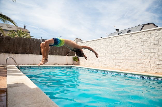 Young fitness man jumping into the water in the pool one day of summer vacation 