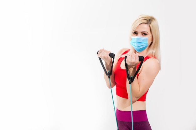 Young fitness sport woman training with trx and wearing disposable medical mask. TRX concept isolated on white background.