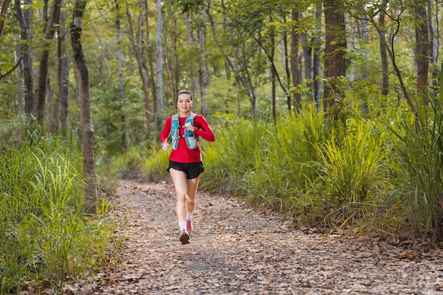 Young fitness sportswoman trail runner running in the tropical forest park in the evening