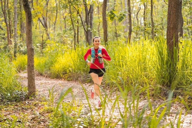 Young fitness sportswoman trail runner running in the tropical forest park in the evening