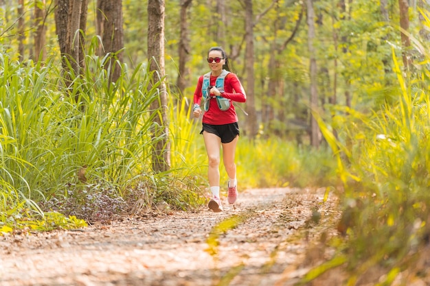 Young fitness sportswoman trail runner running in the tropical forest park in the evening