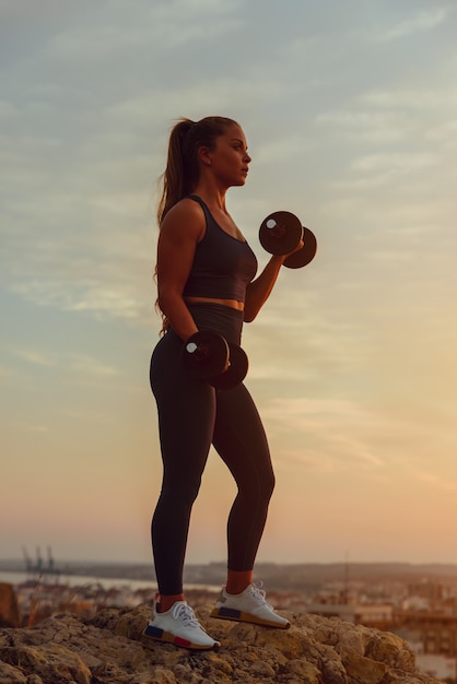 Young fitness woman lifts weights outdoors