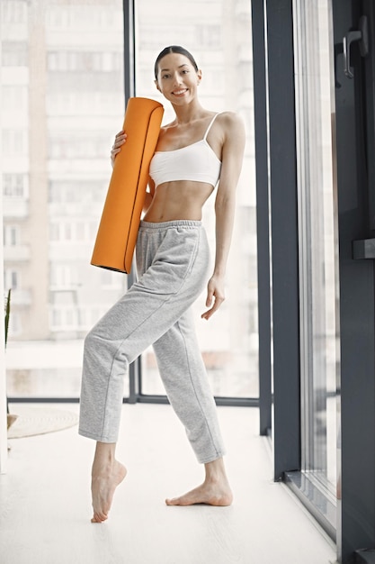 Young fitness woman ready for workout holding orange yoga mat