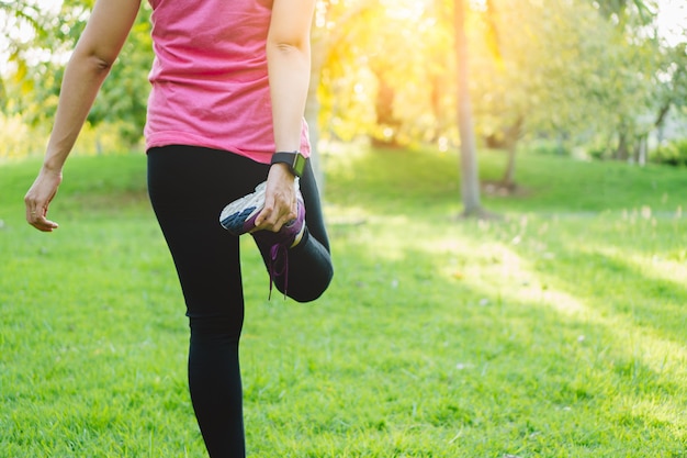 Young fitness woman runner stretching her legs before run and workout in park.