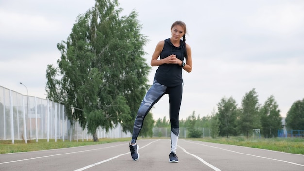 Young fitness woman runner stretching legs on stadium track.