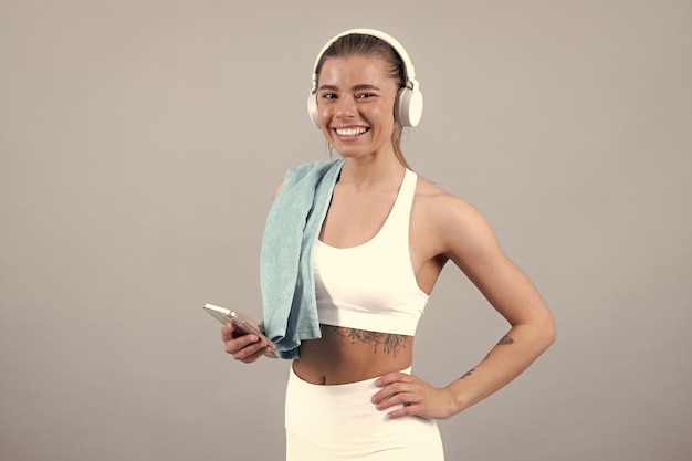 Young fitness woman runner with headphone and towel isolated on gray background Dynamic movement