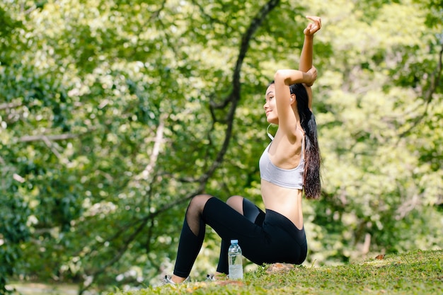 Young fitness woman stretching body under tree.