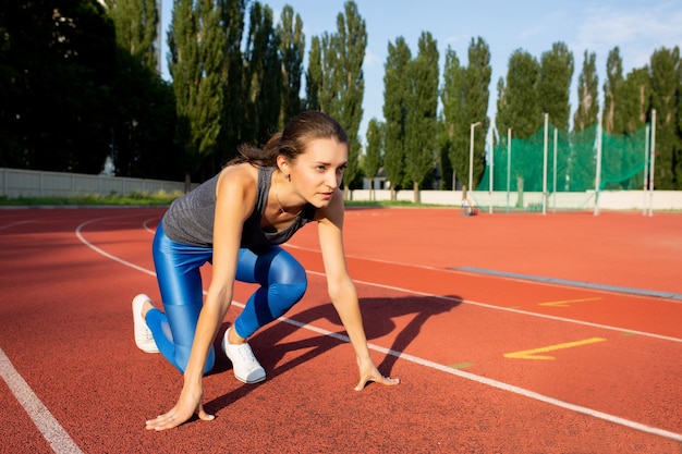 Young fitness woman waiting for start of race on a stadium.  Space for text