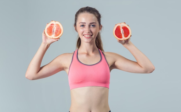 Young fitness woman with grapefruit in hands on light gray 