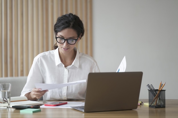 Young focused Italian businesswoman in formal wear analyzing documents reading project statistics