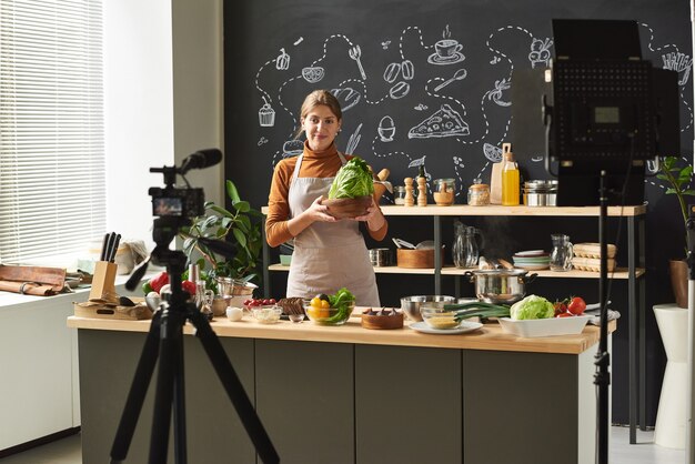 Young food blogger holding vegetable in her hands recording a video on the camera she running her blog