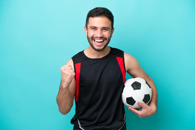 Young football player Brazilian man isolated on blue background celebrating a victory in winner position