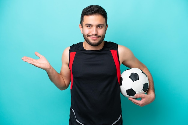 Young football player Brazilian man isolated on blue background having doubts while raising hands