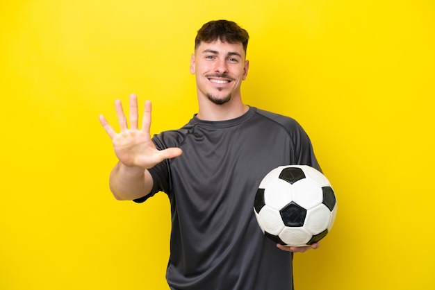 Young football player man isolated on yellow background counting five with fingers