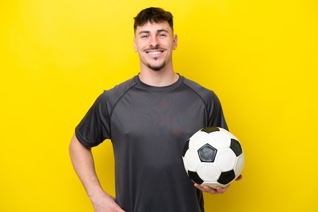 Young football player man isolated on yellow background posing with arms at hip and smiling