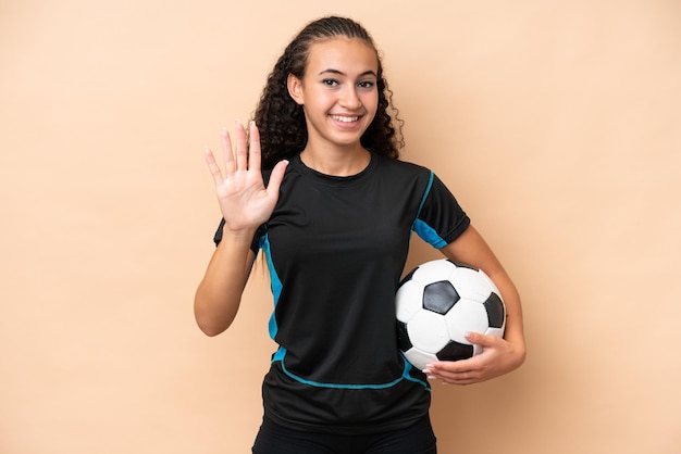 Young football player woman isolated on beige background counting five with fingers