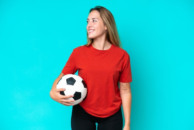 Young football player woman isolated on blue background looking side