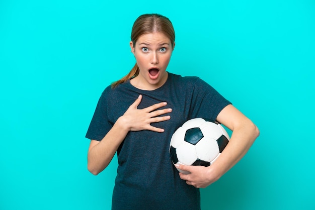 Young football player woman isolated on blue background surprised and shocked while looking right