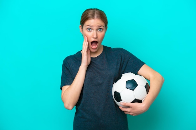 Young football player woman isolated on blue background with surprise and shocked facial expression