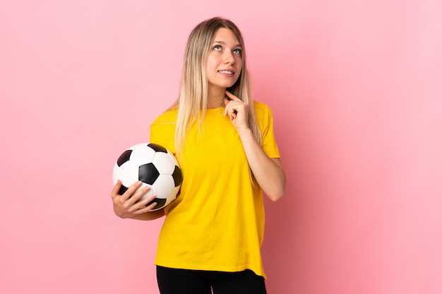 Young football player woman isolated on pink wall thinking an idea