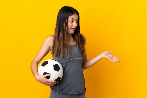 Young football player woman isolated on yellow with surprise expression while looking side