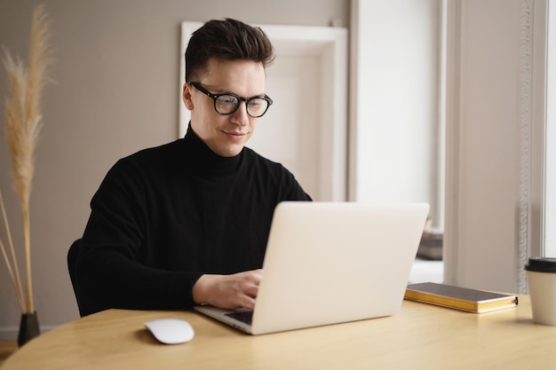 A young freelance man working at a workplace uses a laptop prints an online text message