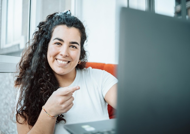 Young freelancer woman working and poiting his finger to computer while working and preparing his day. Concept of remote work from home, getting ready, new job smiling to camera