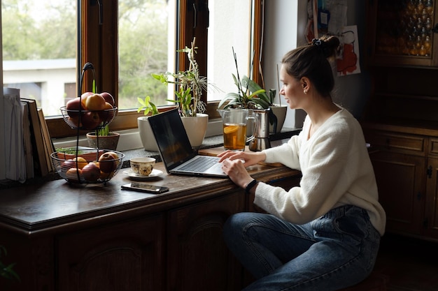 Photo young freelancer working on laptop at home woman using computer on the kitchen for work distant