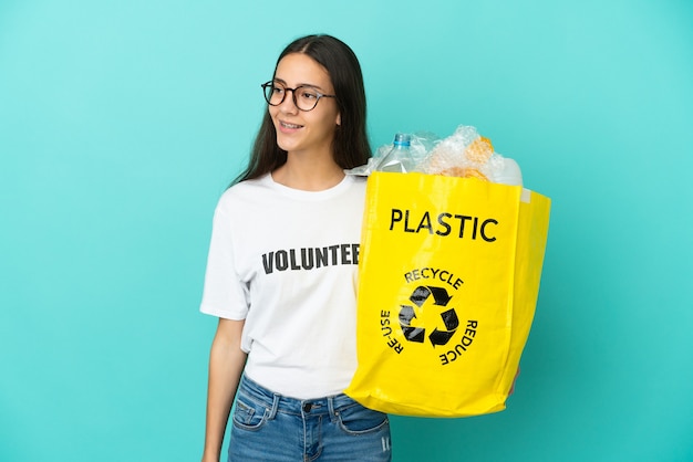 Young French girl holding a bag full of plastic bottles to recycle looking to the side and smiling