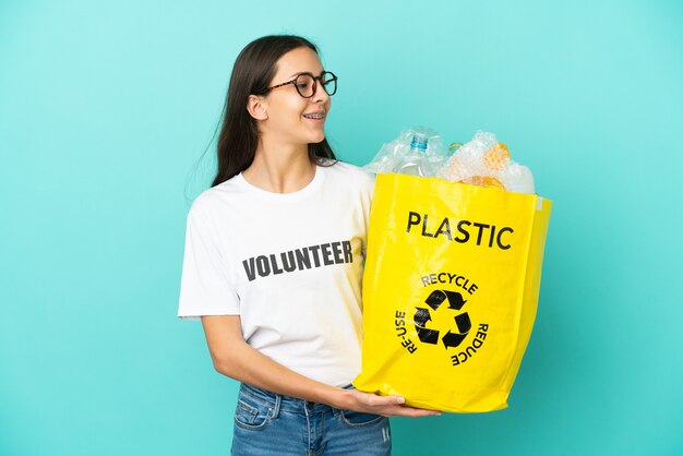 Young French girl holding a bag full of plastic bottles to recycle looking side