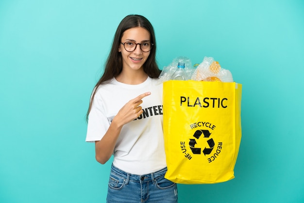 Young French girl holding a bag full of plastic bottles to recycle pointing to the side to present a product