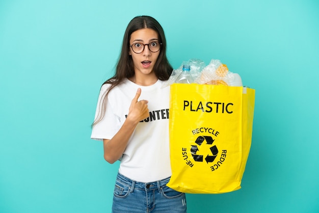 Young French girl holding a bag full of plastic bottles to recycle with surprise facial expression