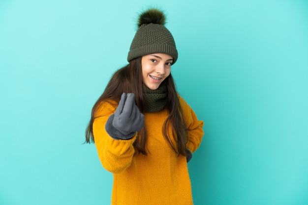 Young French girl isolated on blue background with winter hat making money gesture