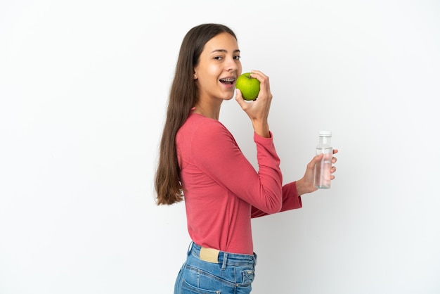 Young French girl isolated on white background with an apple and with a bottle of water