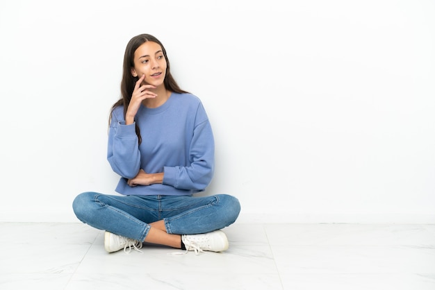 Young French girl sitting on the floor thinking an idea while looking up