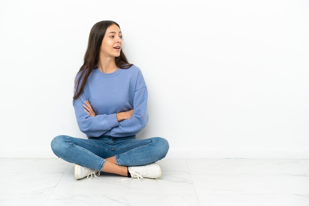 Young French girl sitting on the floor with arms crossed and happy