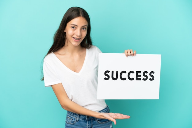 Young French woman isolated on blue background holding a placard with text SUCCESS with happy expression