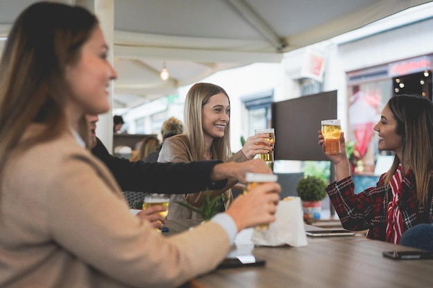 Young friends having fun cheering with beer inside pub restaurant - Focus on center girl face